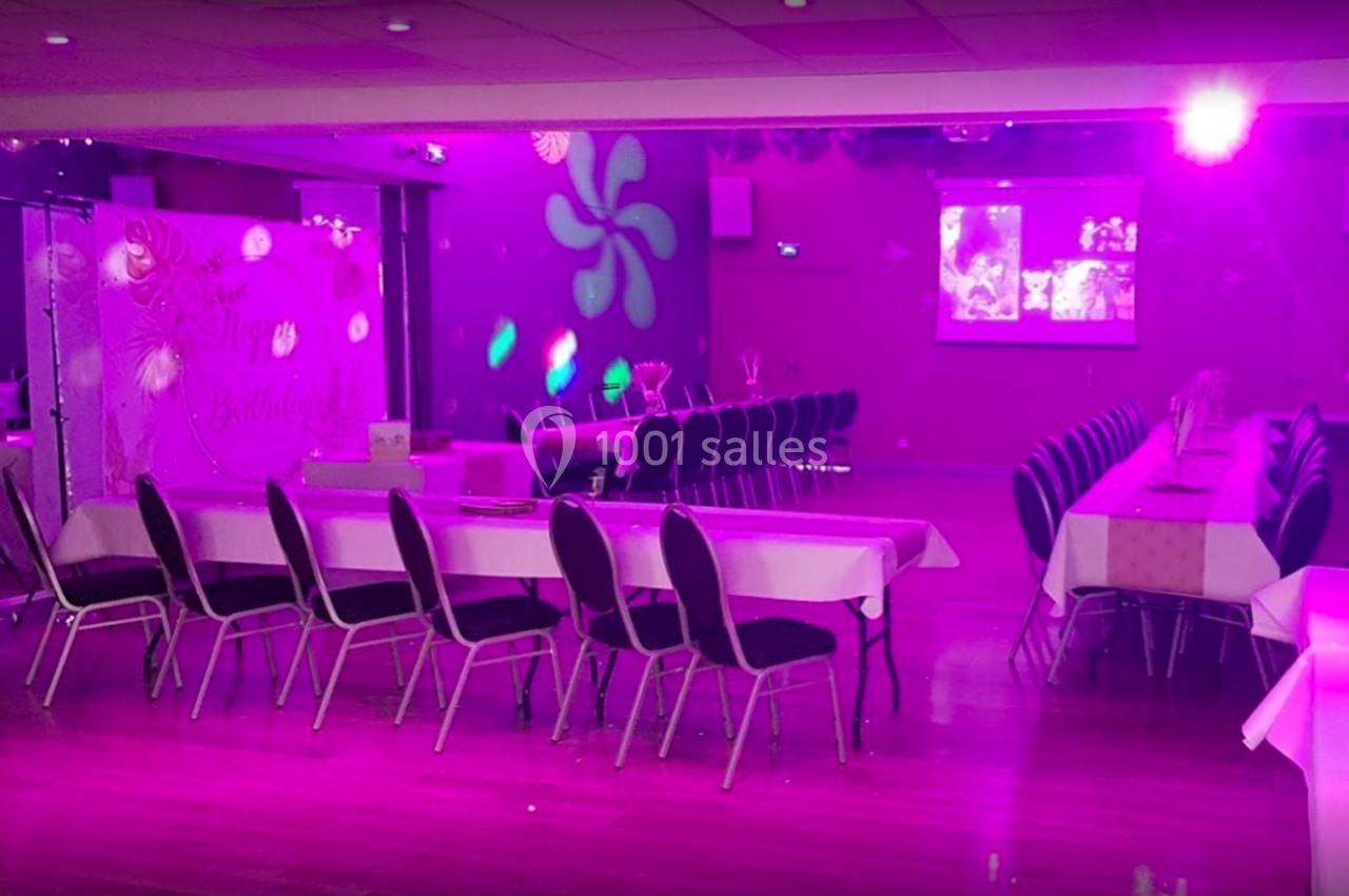 Salle décorée avec des tables alignées et éclairage rose, prête pour un événement festif ou une réception.