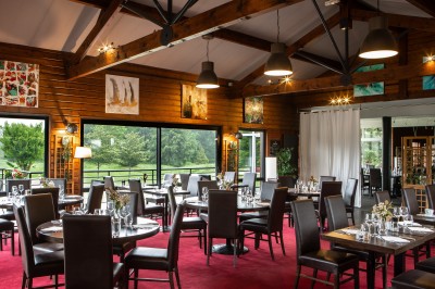 Table dressée en extérieur avec boissons et verres, sur une terrasse en bois surplombant un terrain de golf verdoyant.