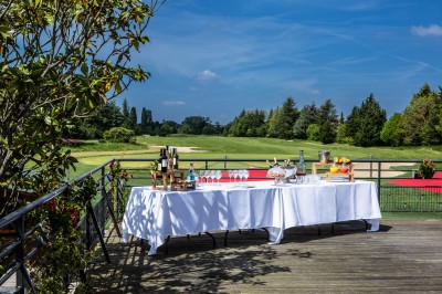 Table dressée en extérieur avec boissons et verres, sur une terrasse en bois surplombant un terrain de golf verdoyant.