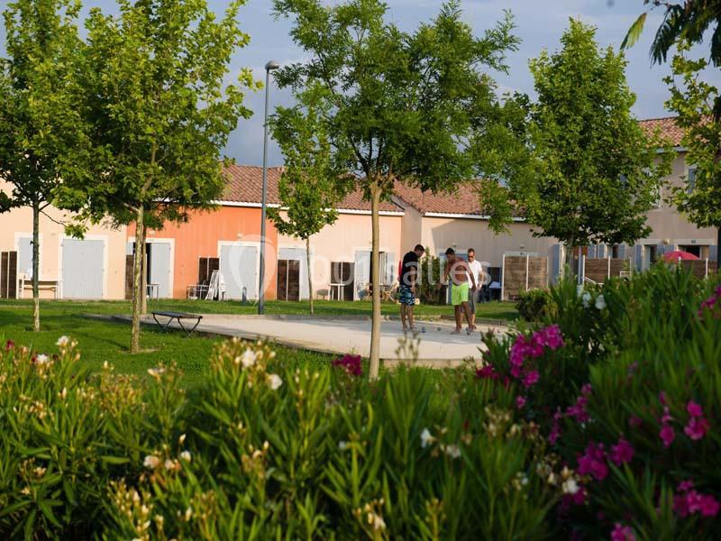 Des personnes marchent dans un espace vert avec des arbres, des fleurs et des bâtiments en arrière-plan.