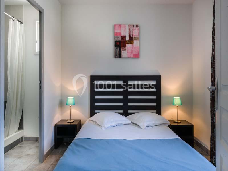 Lit double avec drap bleu dans une chambre lumineuse, encadrée par deux tables de chevet avec lampes allumées.