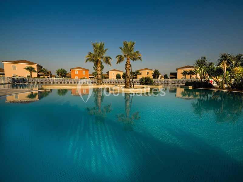 Vue d'une piscine calme entourée de palmiers et de maisons aux façades colorées sous un ciel dégagé.