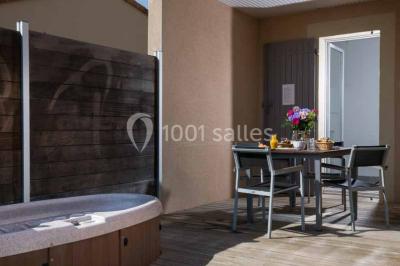 Salle à manger lumineuse avec table en bois, chaises colorées, cuisine ouverte et décoration sobre.