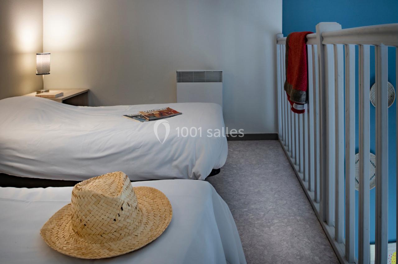 Deux lits simples avec draps blancs dans une chambre lumineuse, un chapeau de paille posé sur l'un d'eux.