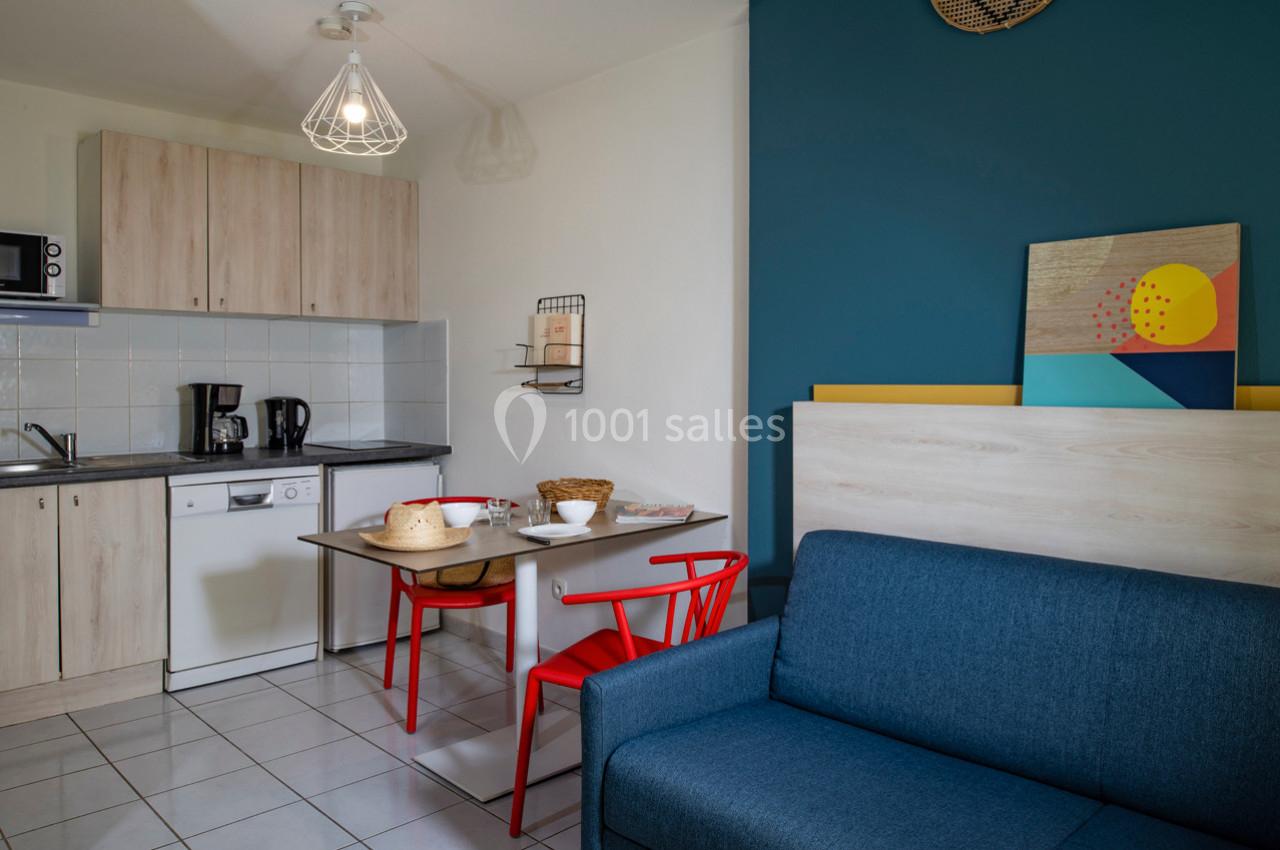 Cuisine ouverte avec table à manger, chaises rouges, canapé bleu et décoration murale colorée.