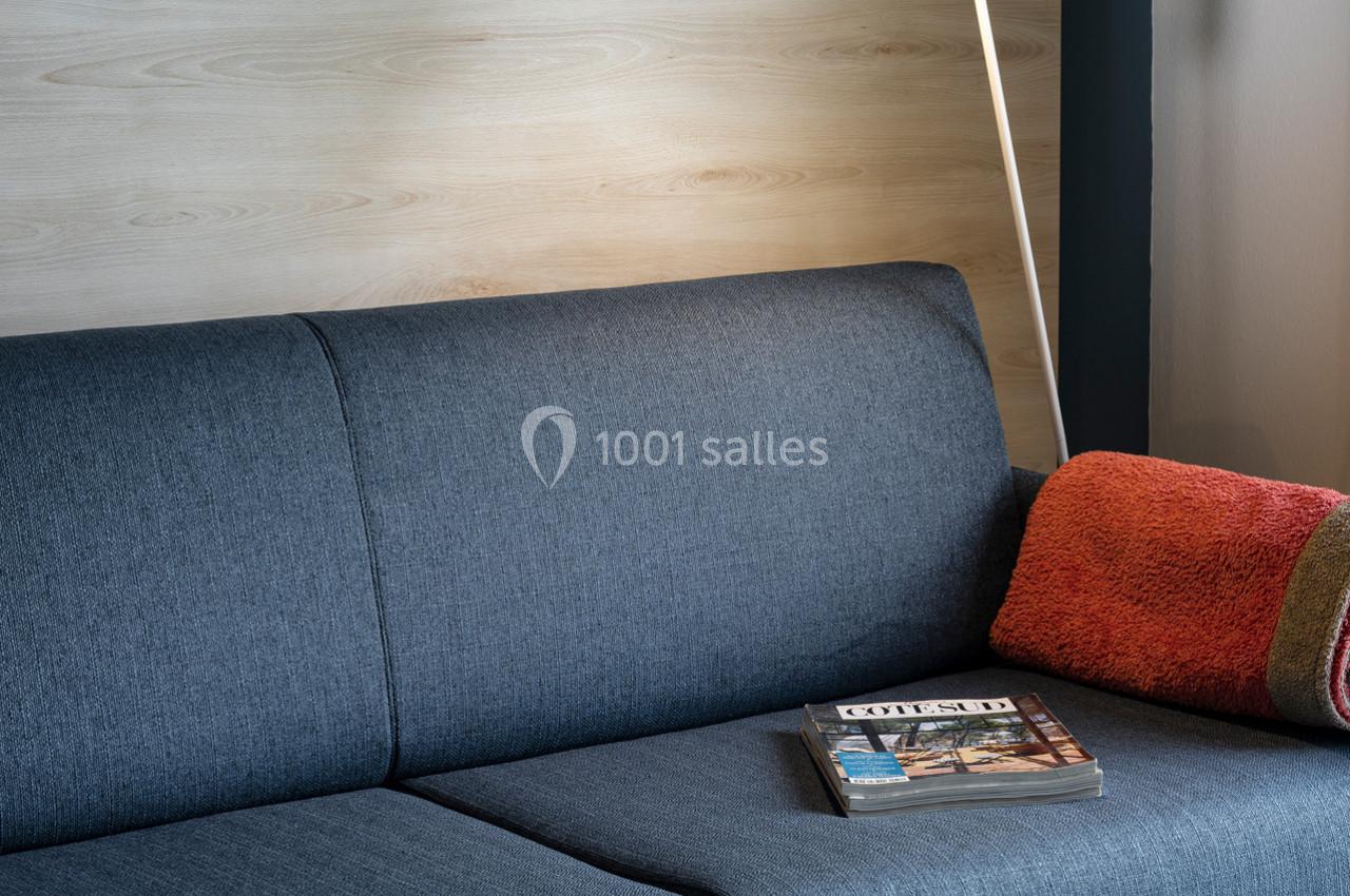 Canapé gris avec appui-tête en bois clair, coussin orange et magazine posé sur l'assise.