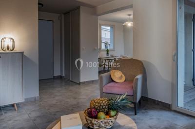 Salle à manger lumineuse avec table en bois, chaises colorées, cuisine ouverte et décoration sobre.