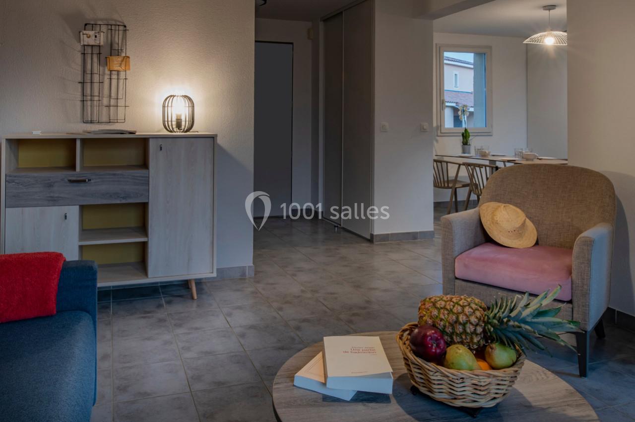 Salon lumineux avec mobilier moderne, corbeille de fruits sur une table basse et vue sur une salle à manger adjacente.