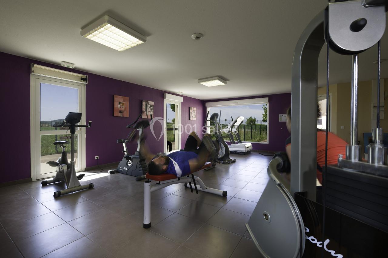 Salle de sport lumineuse avec équipements de fitness, un homme allongé sur un banc effectue un exercice.