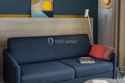 Salle à manger lumineuse avec table en bois, chaises colorées, cuisine ouverte et décoration sobre.