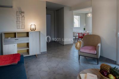 Salle à manger lumineuse avec table en bois, chaises colorées, cuisine ouverte et décoration sobre.