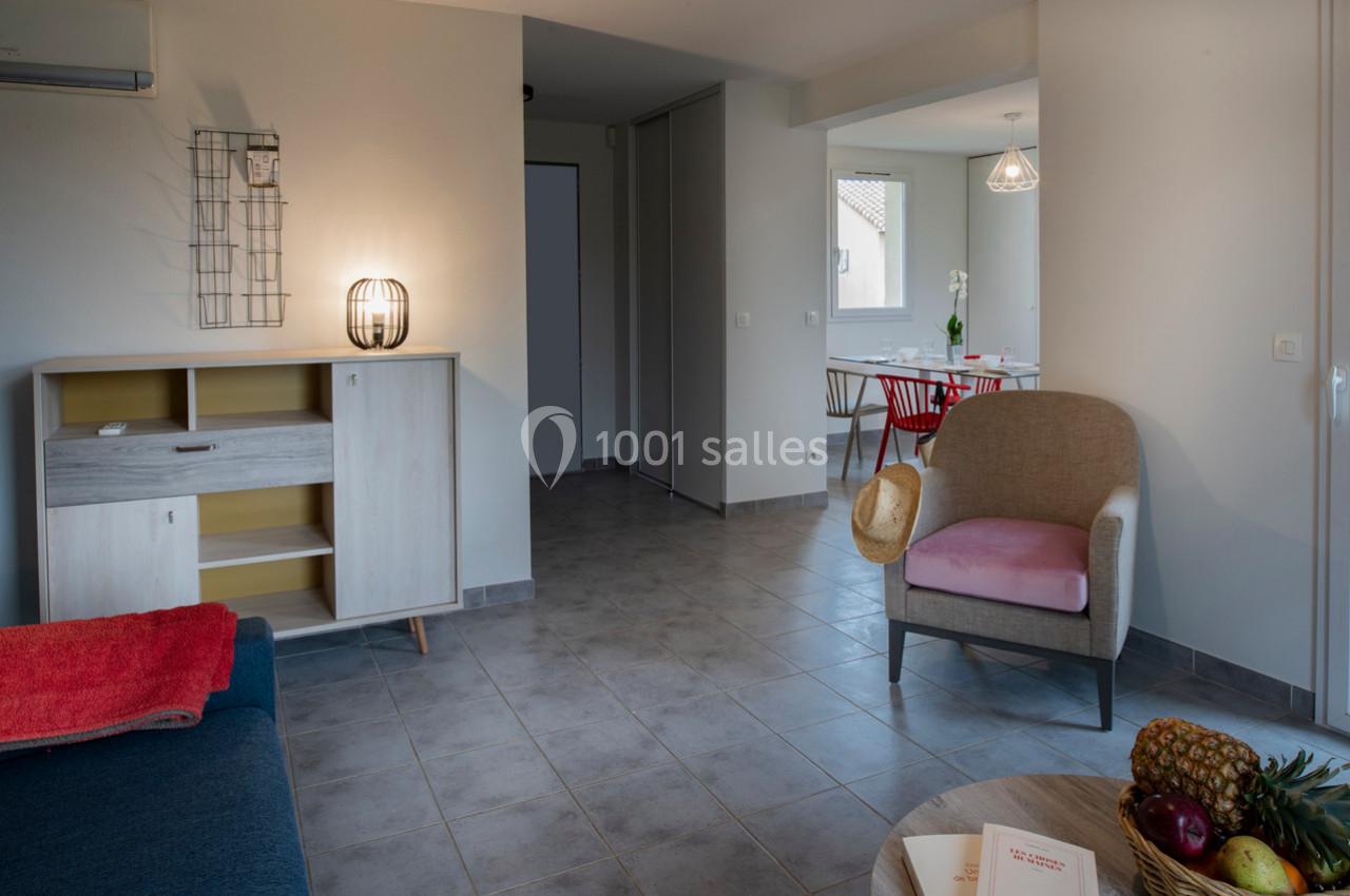 Salon lumineux avec mobilier moderne, fauteuil beige, table à manger et décoration minimaliste sur carrelage gris.