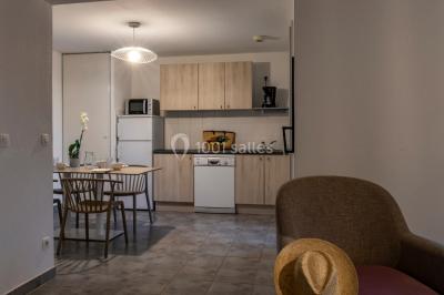 Salle à manger lumineuse avec table en bois, chaises colorées, cuisine ouverte et décoration sobre.