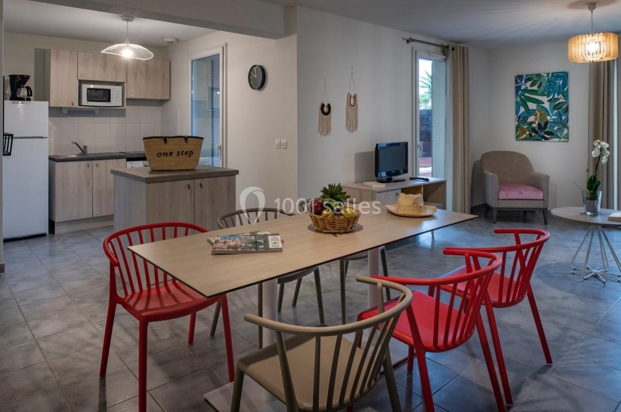 Salle à manger et salon modernes avec table, chaises colorées, cuisine équipée et décoration chaleureuse.