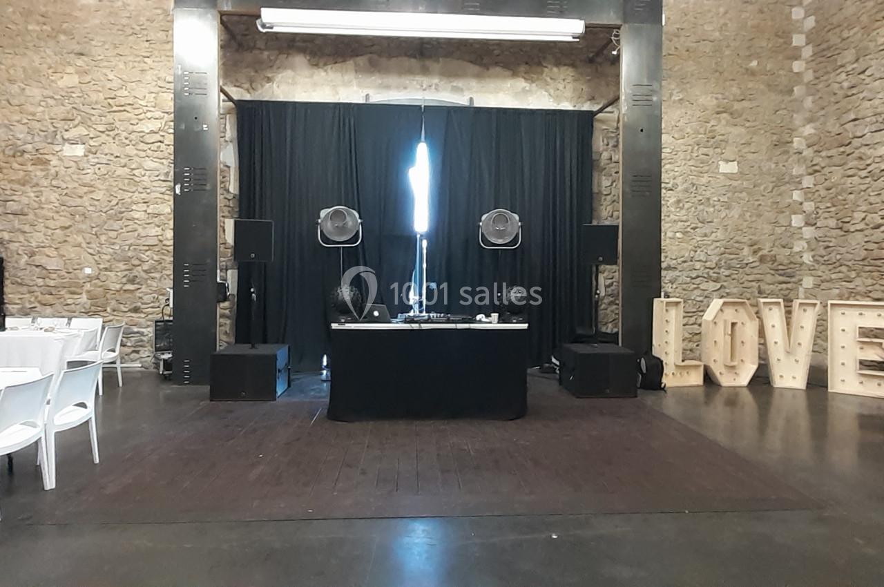 Salle de réception en pierre avec tables dressées, espace DJ central et lettres lumineuses formant ’LOVE’.