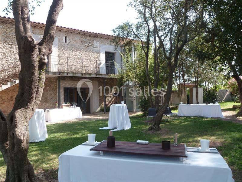 Espace extérieur avec tables dressées et bâtiment en pierre en arrière-plan, entouré d'arbres et de verdure.