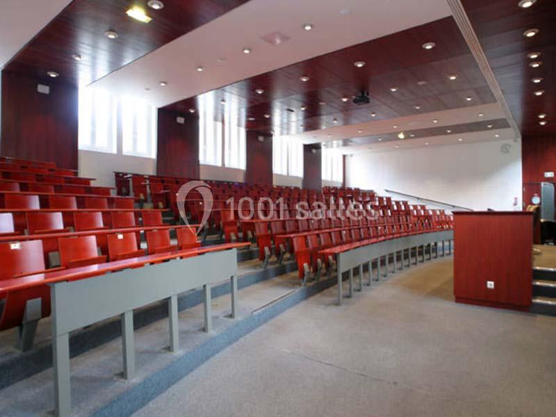 Salle de conférence vide avec des rangées de sièges rouges, un pupitre en bois et un éclairage naturel provenant des…