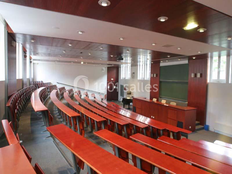 Salle de cours vide avec des rangées de tables en bois, un tableau noir et un bureau pour l'enseignant.