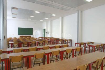 Salle de restauration lumineuse avec de grandes baies vitrées, tables orange et bois, et chaises assorties.
