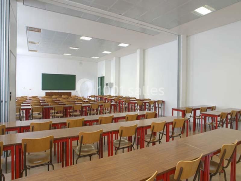 Salle de classe vide avec des rangées de tables en bois, des chaises et un tableau vert au fond.