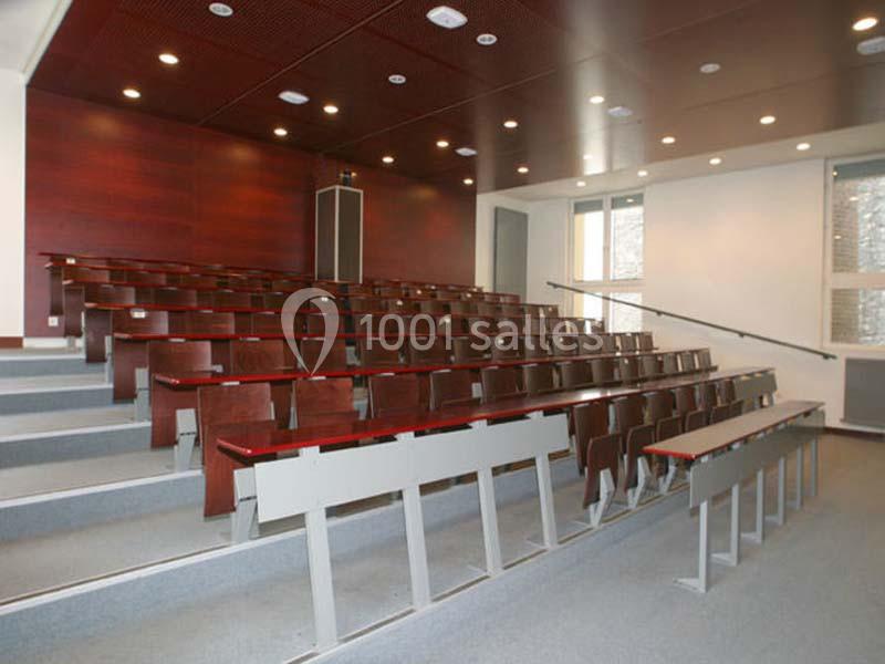 Salle de cours vide avec des rangées de bancs en bois et un éclairage au plafond.