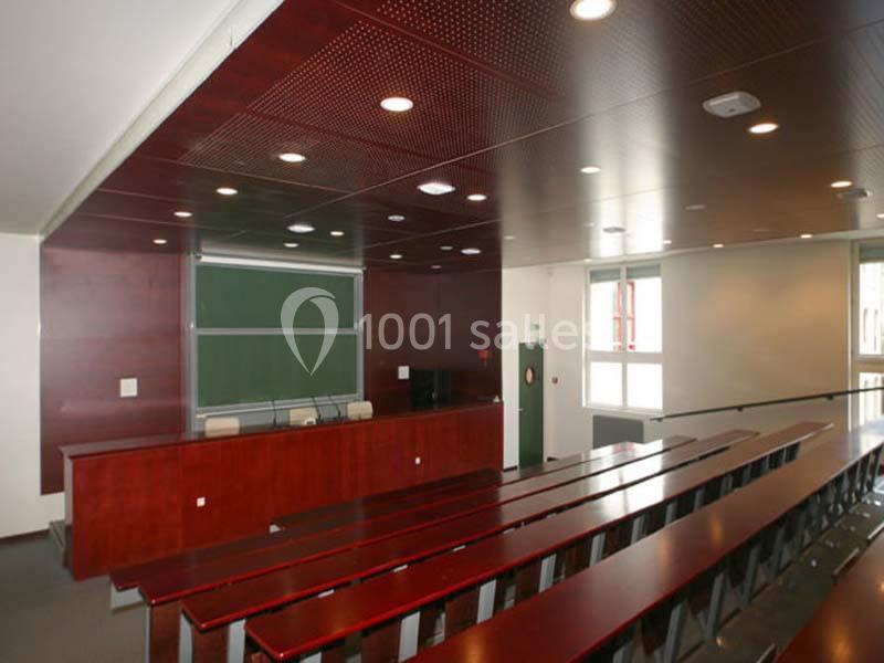 Salle de classe avec rangées de tables en bois, tableau noir et éclairage au plafond.