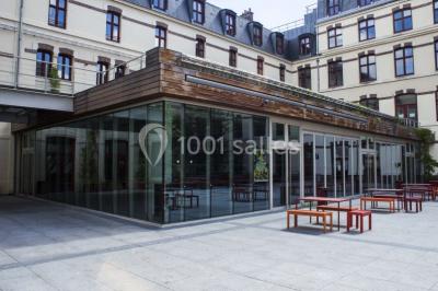 Salle de restauration lumineuse avec de grandes baies vitrées, tables orange et bois, et chaises assorties.