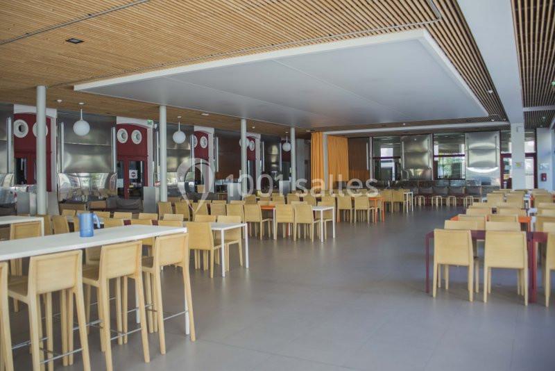 Salle de restaurant spacieuse avec tables et chaises en bois, éclairage naturel et plafond en bois.