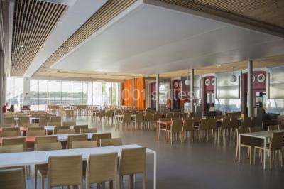 Salle de restauration lumineuse avec de grandes baies vitrées, tables orange et bois, et chaises assorties.