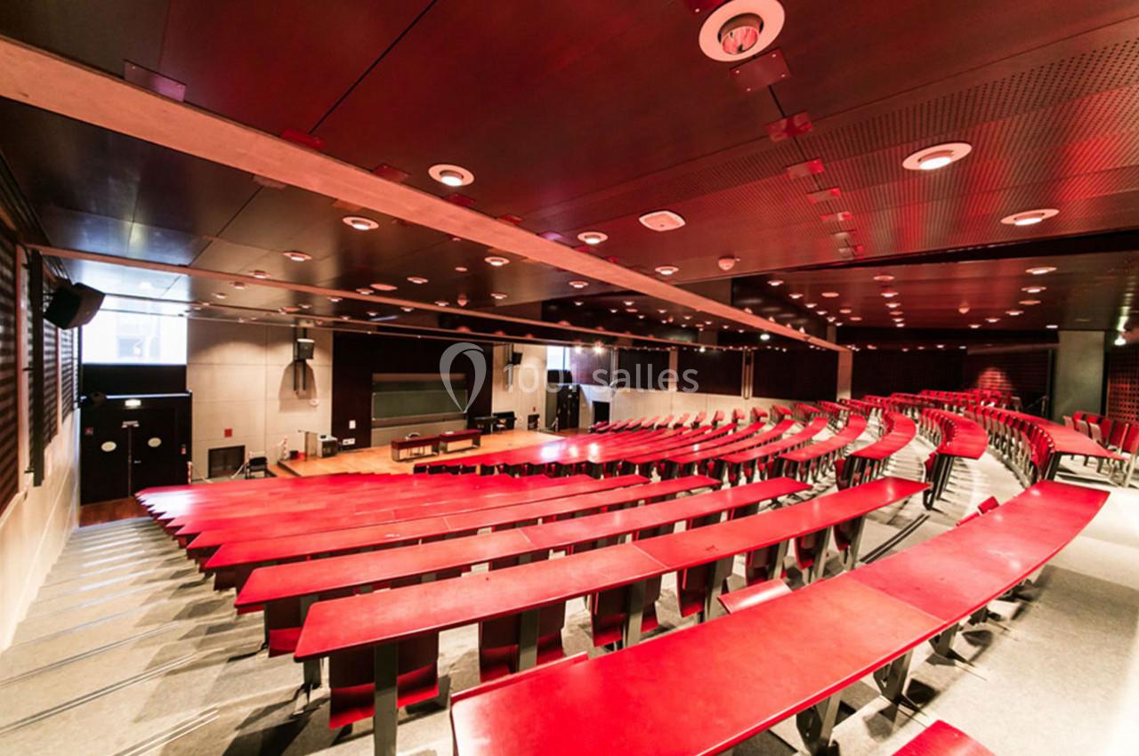 Amphithéâtre moderne avec des rangées de tables rouges et un éclairage intégré, équipé d'un écran et d'un pupitre.