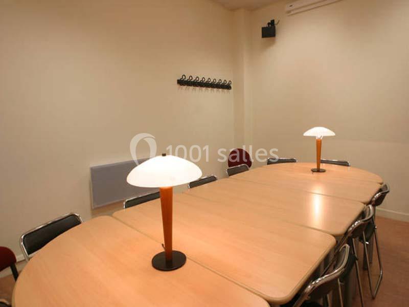 Salle de réunion avec une grande table ovale en bois, entourée de chaises et éclairée par deux lampes de table.