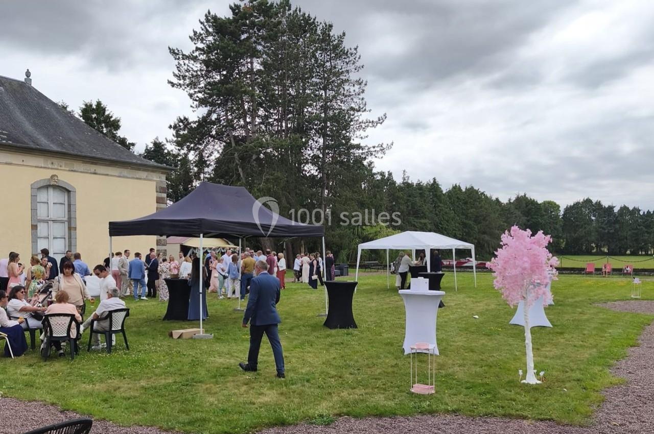 Groupe de personnes rassemblées dans un jardin avec tentes, tables et décorations, devant un bâtiment ancien.