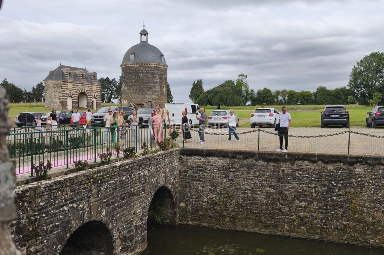 Un groupe de personnes rassemblé près d'un pont en pierre, avec des bâtiments historiques et des voitures en arrière-plan.