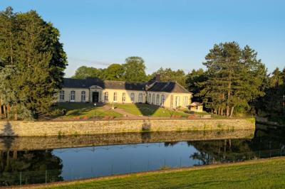 Façade en pierre d'un château bordé par un cours d'eau, avec un pont en arc et des arbres environnants.