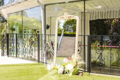 Un photographe capture une cérémonie sous une pergola décorée de fleurs blanches, entourée de verdure et de rochers.
