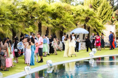 Un photographe capture une cérémonie sous une pergola décorée de fleurs blanches, entourée de verdure et de rochers.