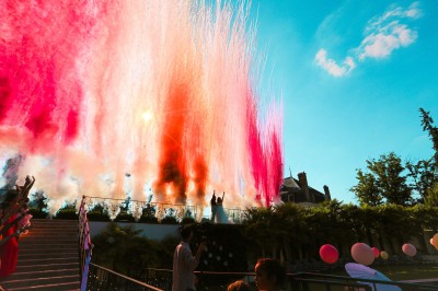 Un photographe capture une cérémonie sous une pergola décorée de fleurs blanches, entourée de verdure et de rochers.