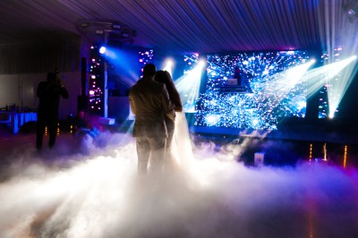 Un photographe capture une cérémonie sous une pergola décorée de fleurs blanches, entourée de verdure et de rochers.