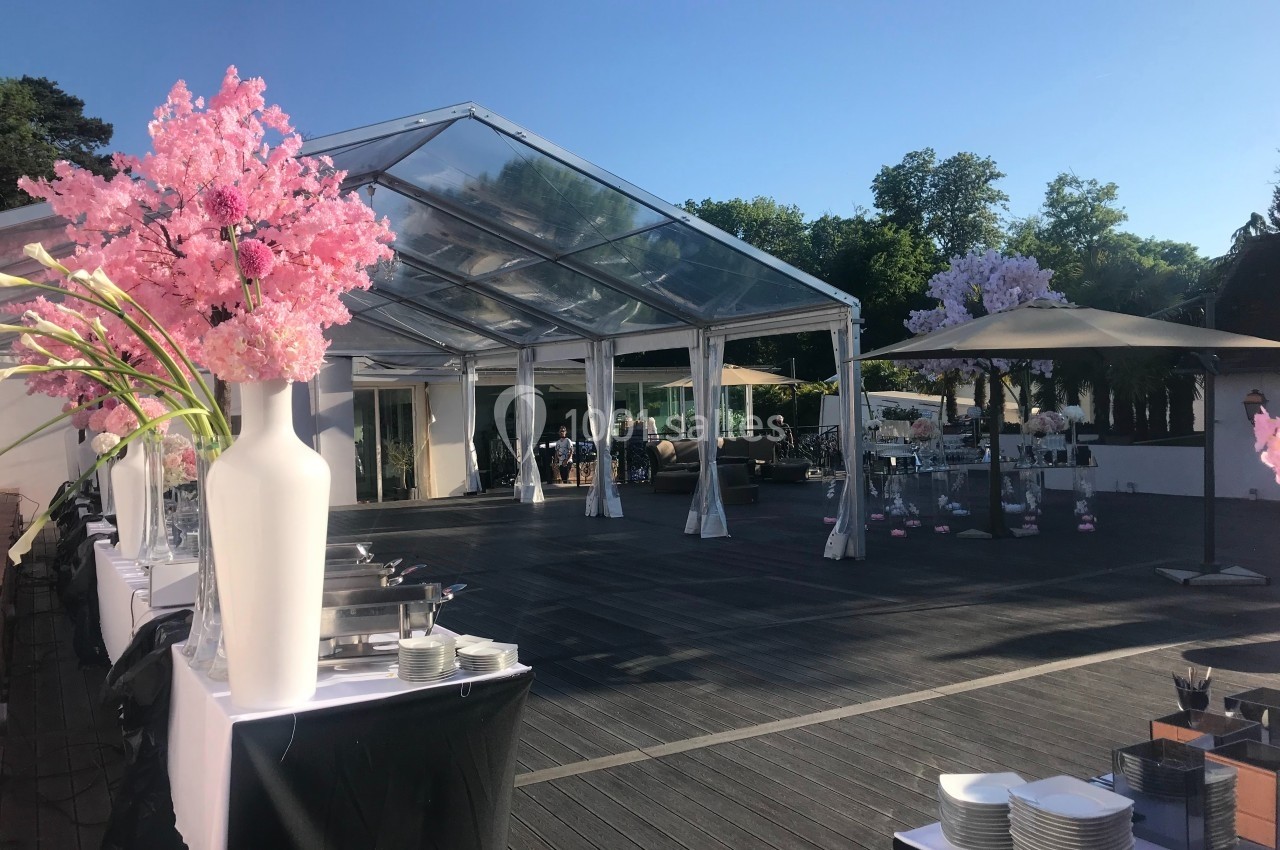 Structure en verre transparente installée en extérieur, entourée de tables dressées et de décorations florales.