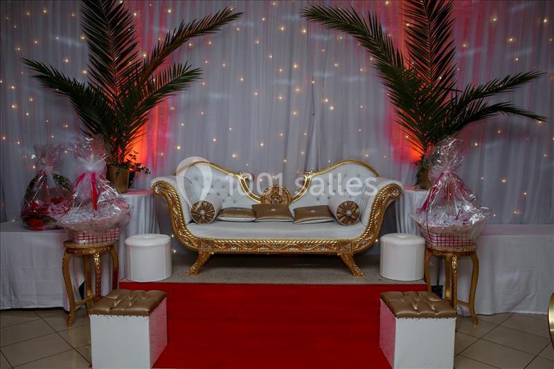 Canapé doré et blanc décoré, entouré de palmiers, de cadeaux emballés et éclairé par des lumières tamisées.