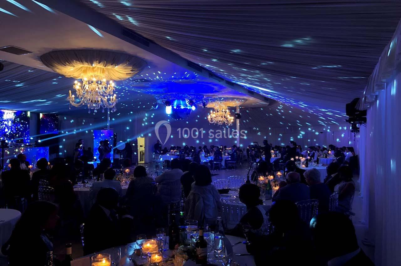 Salle de réception éclairée par des lustres et des lumières bleues, avec des invités assis à des tables décorées.