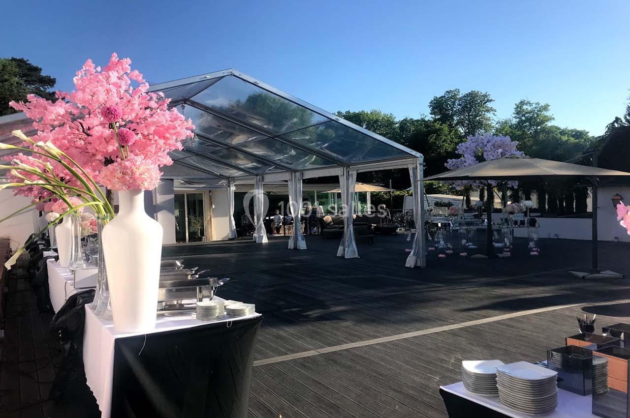 Structure transparente avec tables dressées, décorations florales et espace extérieur sous un ciel dégagé.