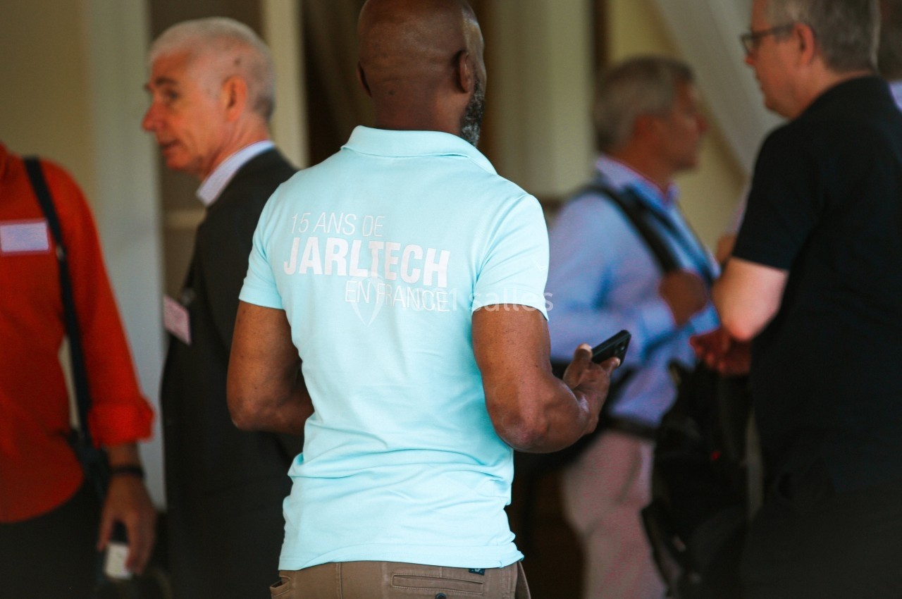 Un homme de dos portant un polo bleu avec l'inscription ’15 ans de Jarltech en France’, entouré de plusieurs personnes.