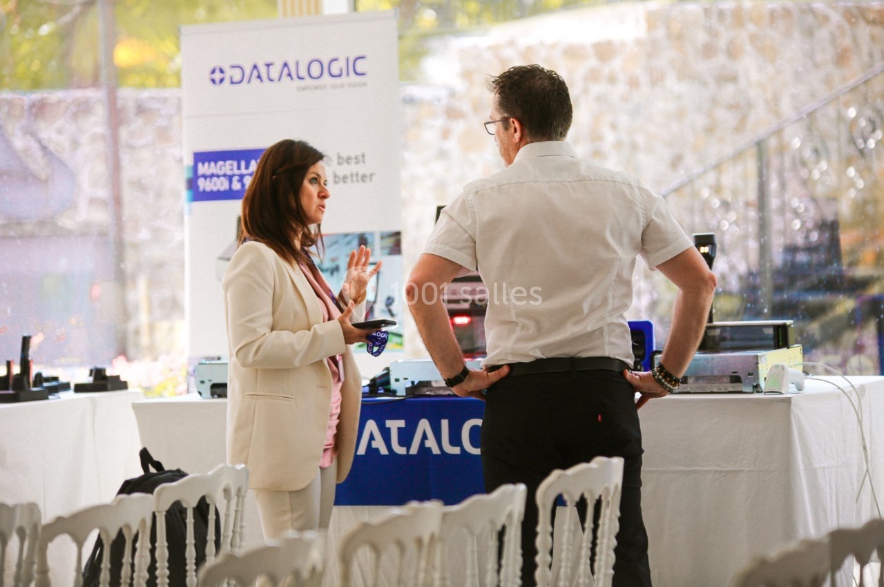Deux personnes discutent devant un stand d'exposition avec des équipements électroniques et des affiches promotionnelles.