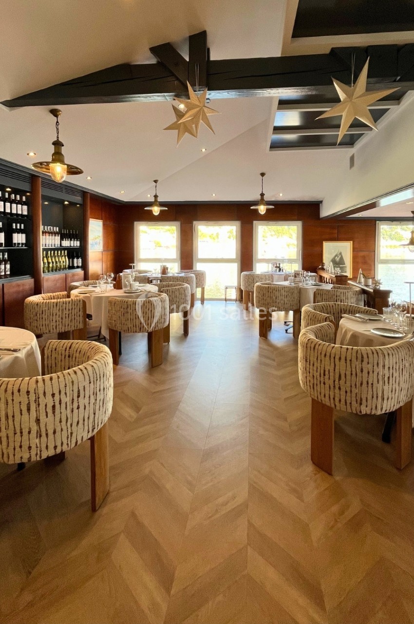 Salle de restaurant lumineuse avec tables dressées, chaises rembourrées et étagères de bouteilles de vin en arrière-plan.