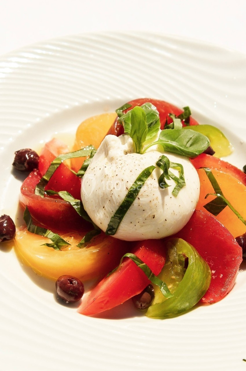 Assiette de burrata garnie de tomates colorées, olives noires et feuilles de basilic frais.