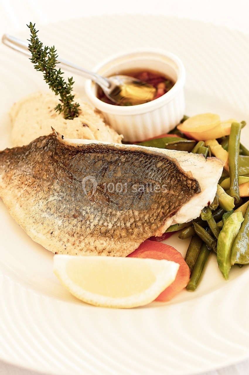 Filet de poisson grillé servi avec légumes sautés, purée et une sauce dans un ramequin, décoré d'une branche de thym.