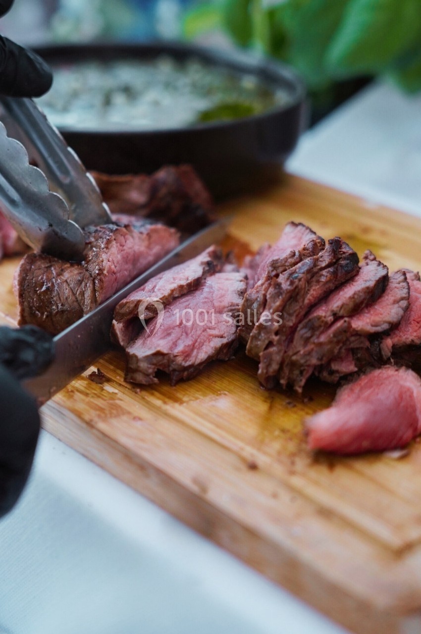 Tranches de viande rouge juteuse découpées sur une planche en bois avec une sauce en arrière-plan.