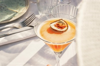 Un couple en tenue élégante regarde la mer au coucher du soleil, avec un bateau visible à l'horizon.