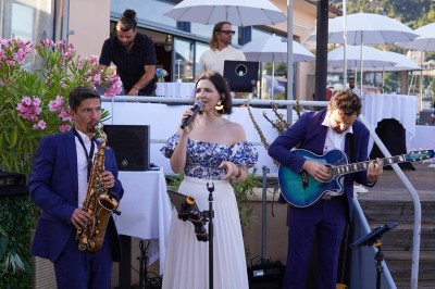 Un couple en tenue élégante regarde la mer au coucher du soleil, avec un bateau visible à l'horizon.